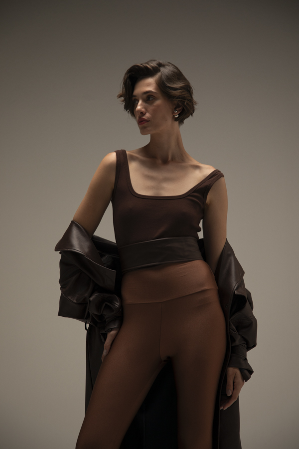 Mulher usando conjunto de top e legging Mocha Mousse, com jaqueta de couro escura sobre os ombros. Ela está em pé, olhando para o lado, com cabelo curto e expressão elegante.