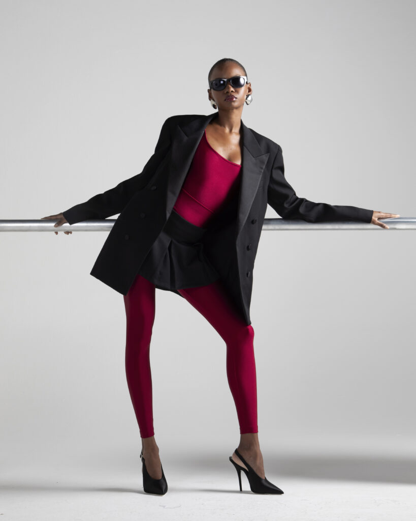 Modelo usando legging em lycra vermelha de alta compressão, modelagem ajustada ao corpo, cintura alta e efeito modelador, combinada com body e blazer oversized preto, em fundo neutro.