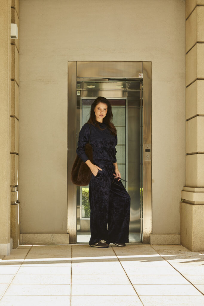 Mulher veste conjunto azul-marinho de veludo com modelagem ampla, combinando conforto e elegância em ambiente externo.