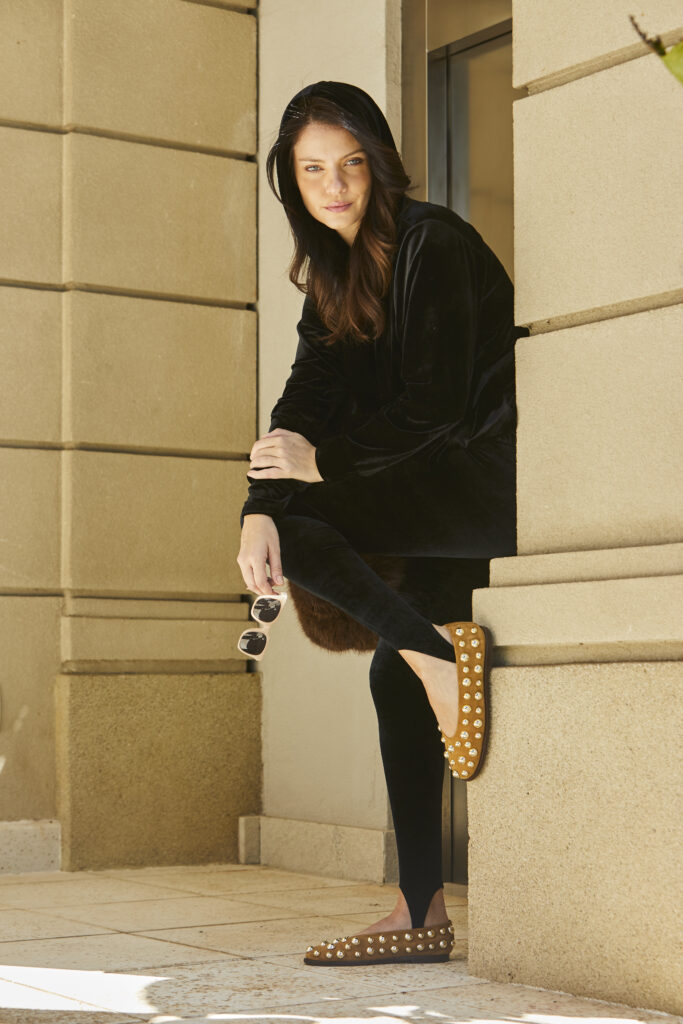Mulher usando conjunto preto de veludo posa em ambiente externo, segurando óculos escuros e destacando um look elegante e confortável.