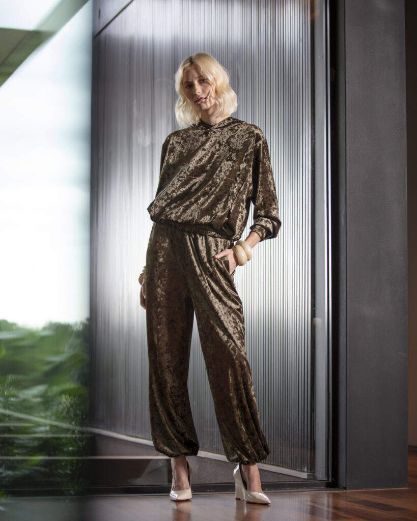Mulher veste conjunto de veludo marrom com blusa e calça, combinando conforto, sofisticação e caimento elegante em ambiente moderno.